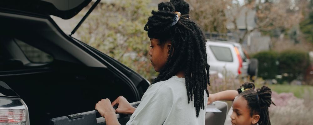 Two children loading luggage into a car trunk before a trip
