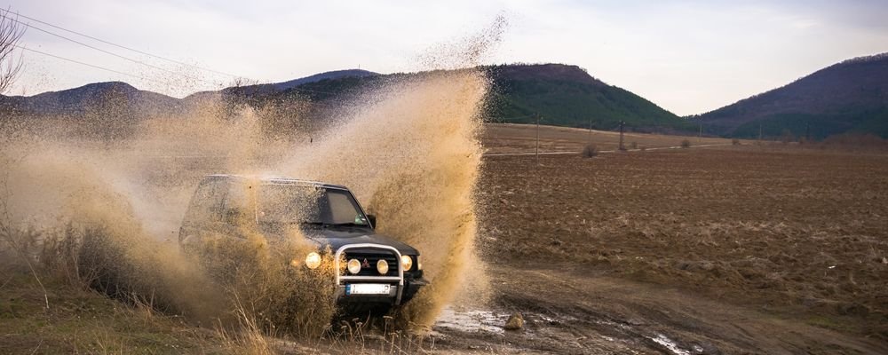 Four-wheel-drive SUV driving through deep mud off road